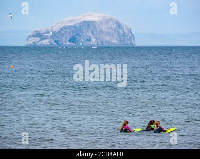 Drei Mädchen im Meer mit Body Boards und Bass Rock Gannet Kolonie am Horizont, Firth of Forth, East Lothian, Schottland, UK Stockfoto