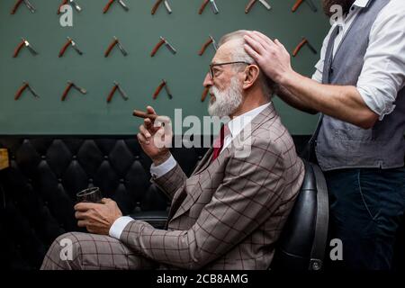 Friseur Bürsten graue Haare von Respektablen alten männlichen Klienten im Maßanzug in der Friseur gekleidet. Stattliche Friseur macht neue Frisur, während eine reiche alte Stockfoto