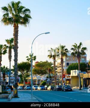 PAPHOS, ZYPERN - 13. FEBRUAR 2019: Stadtbild der Innenstadt von Paphos mit Palmen, Geschäften und Autos im Abendlicht geparkt Stockfoto