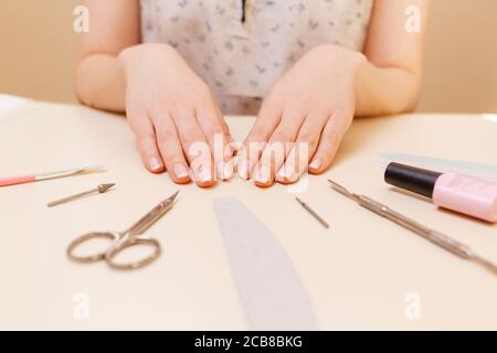 Medizin, Kosmetik und Maniküre. Ein Kunde in einem Nagelstudio zeigt nach dem Eingriff gepflegte Nägel. Weißer Tisch mit Werkzeugen. Nahaufnahme. Stockfoto