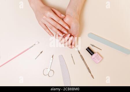 Medizin, Kosmetik und Maniküre. Ein Kunde in einem Nagelstudio zeigt nach dem Eingriff gepflegte Nägel. Weißer Tisch mit Werkzeugen. Nahaufnahme und Stockfoto