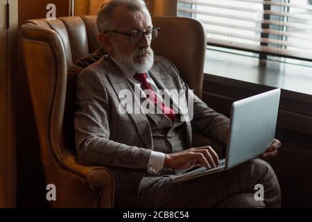 Modisch fokussierten älteren männlichen Schriftsteller trägt Brille und elegante Kleidung auf Laptop arbeiten, Nahaufnahme. Alter Autor, der neue Geschichte während des Sitzens ich verursacht Stockfoto