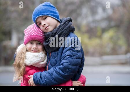 Zwei Kinder, Junge und Mädchen umarmten einander im Freien tragen warme Kleidung in der kalten Herbst oder Winter Wetter. Stockfoto