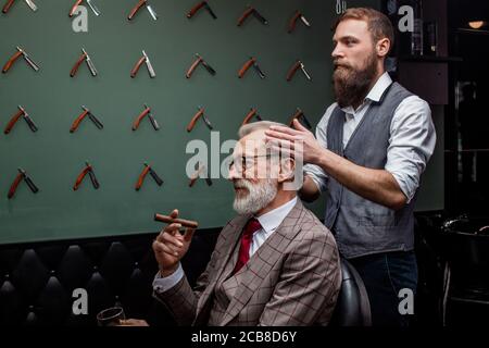 Ältere Menschen besuchen Hairstylist in Friseur. Talanted Haircutter macht Haarschnitt Korrektur im barbershop Salon während Alte - gealterte Client seine ci genießen Stockfoto