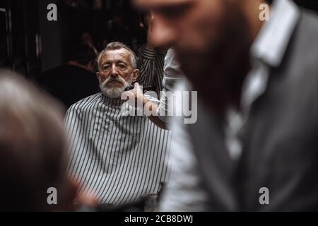 Nahaufnahme eines Friseur s Arbeiten für einen stattlichen respektables Alter-alter bärtiger Mann an der Friseur. Er tut Styling mit dem elektrischen Rasierer. Stockfoto