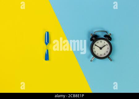 sanduhr mit blauem Sand und schwarzer Uhr in zwei Tönen Hintergrund Stockfoto