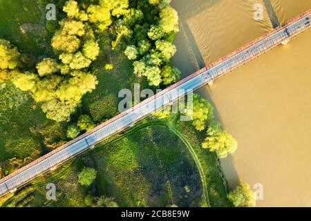 Luftaufnahme einer schmalen Straßenbrücke, die sich über einen schlammigen, breiten Fluss in grüner ländlicher Umgebung erstreckt. Stockfoto