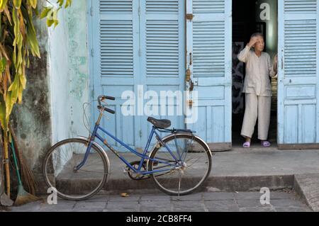 Alte Frau vor ihrer blauen Fensterläden-Tür in Hoi an, Vietnam Stockfoto