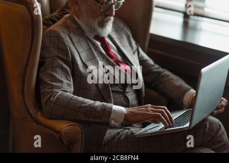 Modisch fokussierten älteren männlichen Schriftsteller trägt Brille und elegante Kleidung auf Laptop arbeiten, Nahaufnahme. Alter Autor, der neue Geschichte während des Sitzens ich verursacht Stockfoto