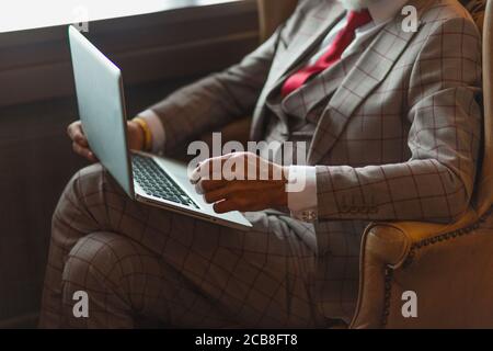 Älteren bärtigen Geschäftsmann in formalen Chic mit Laptop für die Arbeit geeignet während der Sitzung in grosse Leder Sessel in seinem Büro. Stockfoto