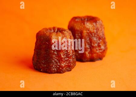 Nahaufnahme von französischem Gebäck Caneles de Bordeaux auf einem Orangefarbener Hintergrund Stockfoto