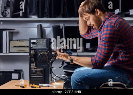 Verwirrt verwirrt Kerl hält viele Drähte und kratzen seinen Kopf, wie er vergessen, wo sie zu verbinden, Nahaufnahme Seitenansicht Foto Stockfoto