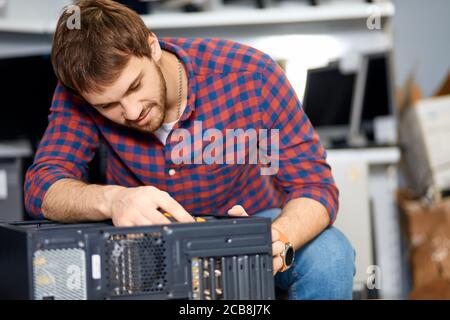 Angenehmer Kerl, der eine alte Systemeinheit auseinandernimmt, Nahaufnahme Foto. Kerl überholen einen Computer im Büro Stockfoto
