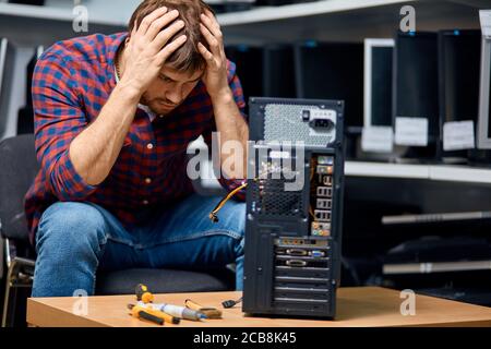 Unglücklicher trauriger Mann mit Händen auf dem Kopf hat einen Computer gebrochen, schlechter Computertechniker hat nicht genug Erfahrung Stockfoto