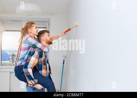 Junges Paar, mit nicht viele für professionelle Maler und Leiter, macht Spaß, als junge Frau Huckepack auf ihren Mann, um zusätzliche Höhe zu gewinnen, wenn p Stockfoto