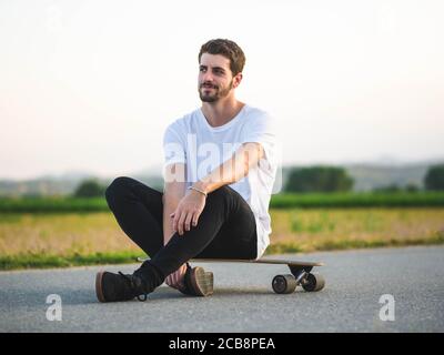 Shallow Focus Aufnahme eines jungen hübschen männlichen Sitzes Ein Skateboard Stockfoto