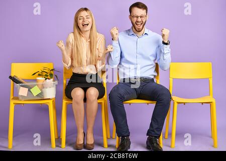 Glückliche junge blonde Frau mit geschlossenen Augen und Mann in Runde Brillen sitzen extrem aufgeregt von großen Nachrichten und warten Für Vorstellungsgespräche Stockfoto