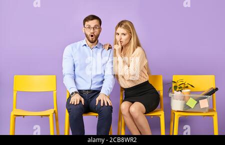 Ziemlich blonde junge Frau hält Finger auf den Lippen zeigt fragen, um das Geheimnis zu halten, junger Mann in Brille erstaunt und schockiert und wartet auf Job Interv Stockfoto