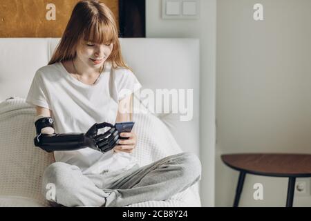 Glückliches Mädchen mit künstlichen Arm Nachrichten senden, sms während der Ruhe zu Hause. Glück, Freizeit, Freizeit Stockfoto