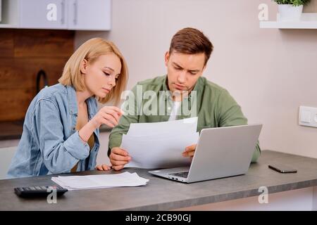 Schöne schöne junge Paar lesen und analysieren Rechnungen sitzen am Tisch und mit modernen Laptop. Junges Paar in beiläufiger Diskussion Hauswirtschaft Stockfoto