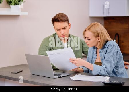 Junge kaukasische Frau und Mann tragen Casual Wear Überprüfung der finanziellen Situation in der Familie, tun Rechnung verficitaion mit Laptop, Papiere und Kalkül Stockfoto