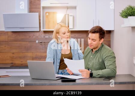 Verwirrt nachdenklich Mann und Frau sitzen zusammen auf dem Tisch, studieren Dokumente ihres Familienunternehmens und arbeiten mit modernen Laptop, Audit zu Hause. Stockfoto