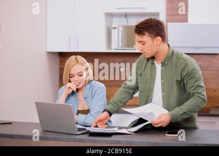 Verwirrt nachdenklich Mann und Frau sitzen zusammen auf dem Tisch, studieren Dokumente ihres Familienunternehmens und arbeiten mit modernen Laptop, Audit zu Hause. Stockfoto