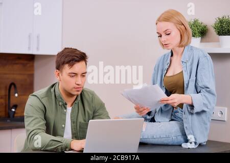 Verwirrt Mann und Frau sitzen zusammen auf dem Tisch zu Hause, studieren Papiere oder Dokumente ihres Familienunternehmens und arbeiten mit modernen Laptop, Audit Stockfoto