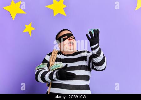 Glücklich verrückt lustig Dieb werfen sein gestohlenes Geld. Räuber in Maske und Handschuhe Spaß mit money.Isolated blauen Hintergrund mit Sternen und Mond. Happ Stockfoto