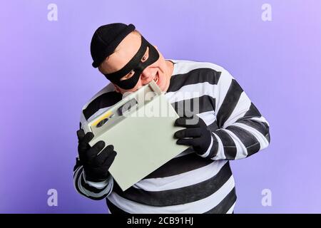 Lustige verrückte Einbrecher in Maske versuchen, sicher mit Zähnen zu öffnen. Close up Portrait. Isolierte blauen Hintergrund. studio erschossen Stockfoto