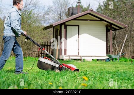 Mann schneidet Gras mit einem Rasenmäher auf dem Hinterhof Stockfoto