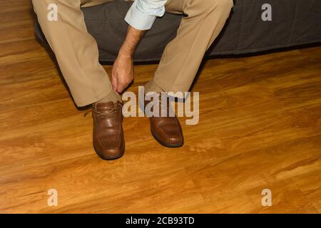 Immer den Tag gehen, kaukasischen Mann sitzen mit beige Slacks und blaues Kleid Hemd setzen auf braunem Kleid Schuh, Beine und Arme Ansicht, loslassen. Stockfoto