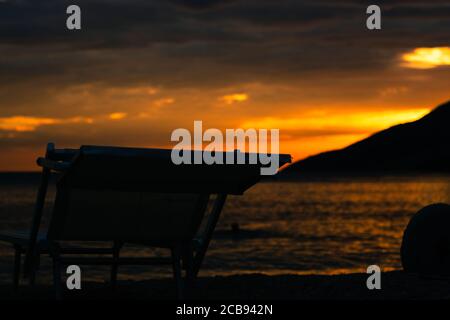 Später leuchtender orangefarbener Sonnenuntergang am Strand Zlatni Rat in Bol. Dunkle Umrisse eines Liegestuhls auf dem Meer, beliebtes Touristenziel in Kroatien. Lebendige Farben Stockfoto