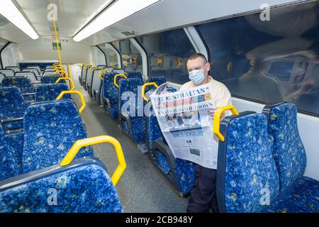 Ein Einzelmann in einem leeren Zug liest Coronavirus-Nachrichten aus der australischen Zeitung „The Australian“ in Sydney, Australien, während die Bevölkerung öffentliche Plätze in Erwartung einer stadtweiten Sperrung verlässt. Viele Geschäfte und Versammlungsorte, die von der Regierung als nicht unbedingt notwendig eingestuft wurden - wie Pubs, Restaurants, Strände und Kultstätten - wurden bis auf weiteres als außer Betrieb gesetzt. (Modell Freigegeben) Stockfoto