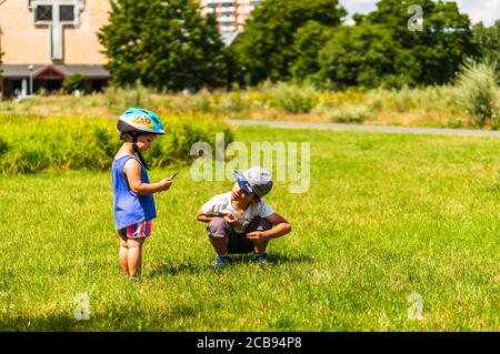 POZNAN, POLEN - 26. Jul 2020: Kleines Mädchen mit Helm zeigt dem Jungen etwas auf einem Grasfeld in einem Park. Stockfoto
