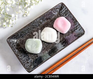 Blick von der Spitze der verschiedenen Geschmacksrichtungen von Mochi auf Eine schwarze rechteckige Platte und Baby Breath Blumen Hintergrund Weichzeichnung Stockfoto