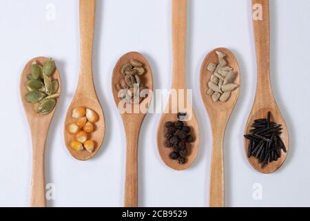 Verschiedene Samen -Mais, Kürbis, Kaffee, Pfeffer, Reis, Sonnenblumen- in Holzlöffeln auf einer weißen Oberfläche Stockfoto