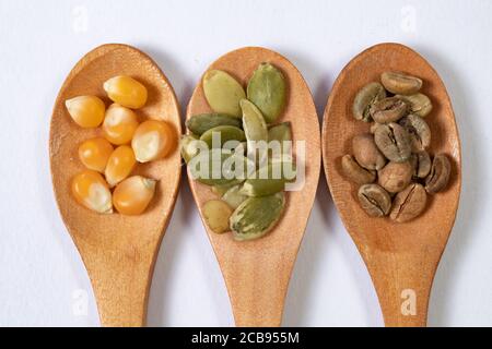 Verschiedene Samen -Mais, Squash, Kaffee- in Holzlöffeln auf einer weißen Oberfläche Stockfoto