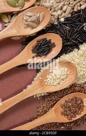 Verschiedene Samen -Quinoa, Kürbis, Reis, Sonnenblume- in Holzlöffeln auf einer Oberfläche von verschiedenen Samen und braunen Hintergrund Stockfoto
