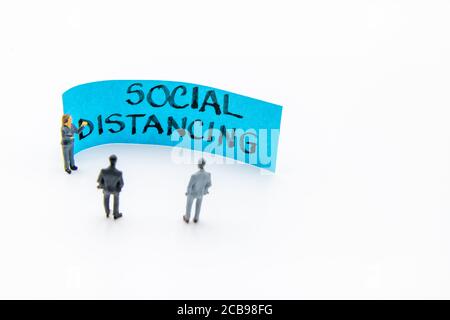 Präsentationstreffen mit Miniaturfiguren, die als Geschäftsleute stehen Vor der Post-it-Notiz mit handgeschriebener Social Distancing-Nachricht Zoll Stockfoto