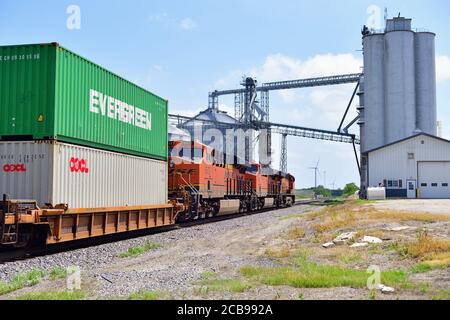 Ransom, Illinois, USA. Burlington Northern Santa Fe Lokomotiven führen einen intermodalen oder Stapelzug in Richtung eines großen Bauernkooperationskomplexes. Stockfoto