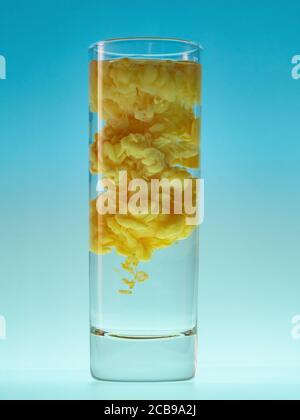 Gelbe Acrylfarbe in Wasser. Abstrakte Farbwolke in Glas Wasser auf blauem Hintergrund Stockfoto