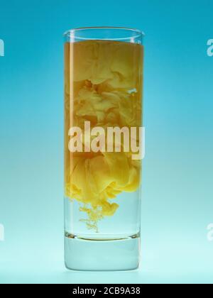 Gelbe Tintenwolke im Glas Wasser. Studioaufnahme. Malen Sie in Wasser auf blauem Hintergrund. Stockfoto