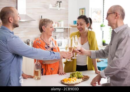 Familie macht einen Toast in der Küche mit Wein. Verschiedene Chees auf Holzplatte. Stockfoto