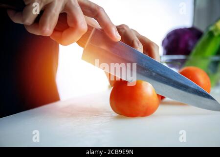 Nahaufnahme Hände Frauen halten Messer und schneiden frische Zucchini auf Schneidebrettchen. Weibliche Hand schneidet rohe japanische Gurke in Kreise mit Messer auf Cu Stockfoto