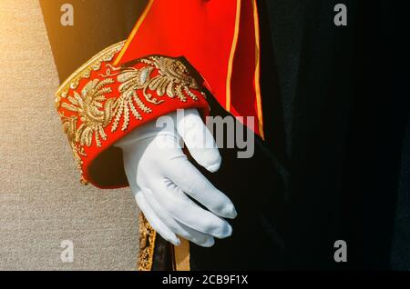 Schwarze historische Herrenbekleidung mit rot und Gold gemusterten Einsätzen am Ärmel, eine Hand in weißen Handschuhen Stockfoto