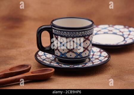 Tassen und Teller Kaffee mit einem traditionellen Design und Holzlöffel mit braunem Hintergrund Stockfoto