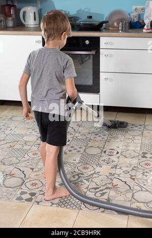 Vorschuljunge hilft seiner Mutter, macht Hausaufgaben, saugt Küchenboden Stockfoto