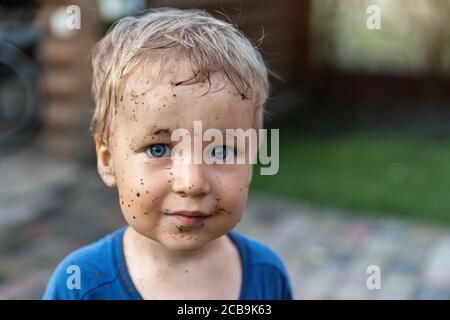 Niedliche liebenswert blonde kaukasischen kleinen glücklich Kleinkind Junge Porträt mit chaotisch Mus Flecken auf Gesicht nach dem Spielen Bewässerung Garten auf Hof oder Grafschaft Bauernhof Stockfoto