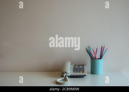 Telefon und Pastellstifte im blauen Glas auf dem Schreibtisch mit grauem Wandhintergrund Stockfoto